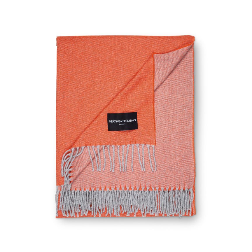 Orange throw blanket with gray fringe and a brand label on a white background