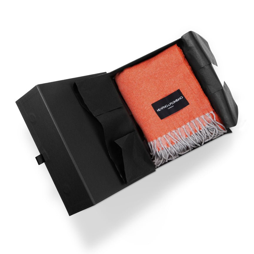 Orange blanket with white fringe in a black packaging box on a white background