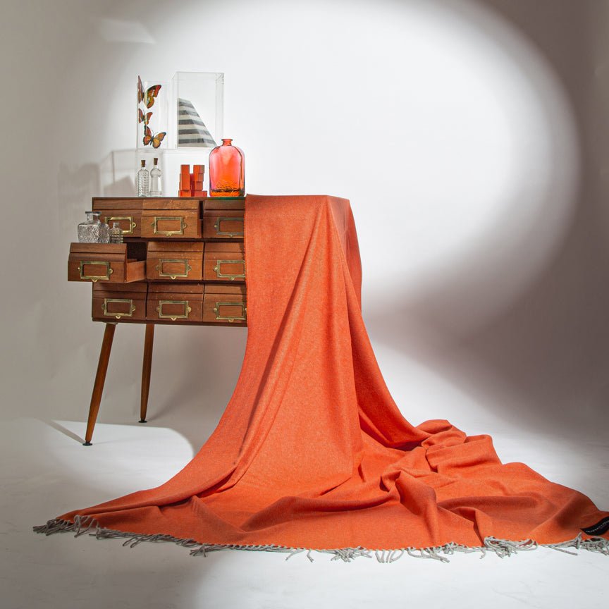 Wooden sideboard with an orange blaket draped over it on a white background