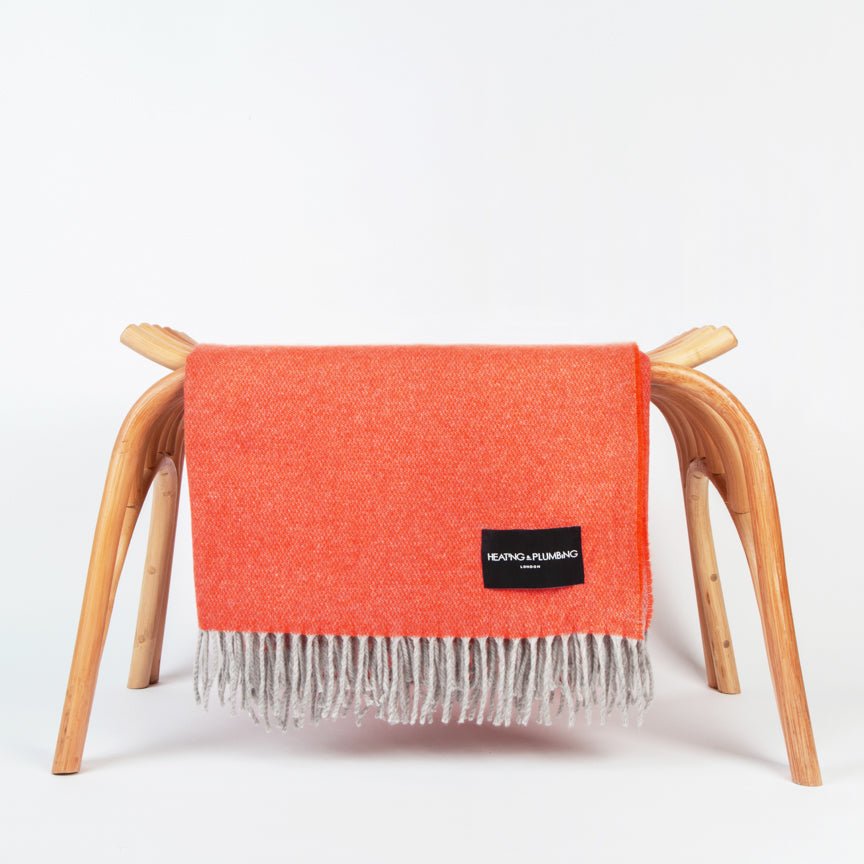 Orange throw blanket with a brand label Heating and Plumbing draped over a wooden stool on a white background