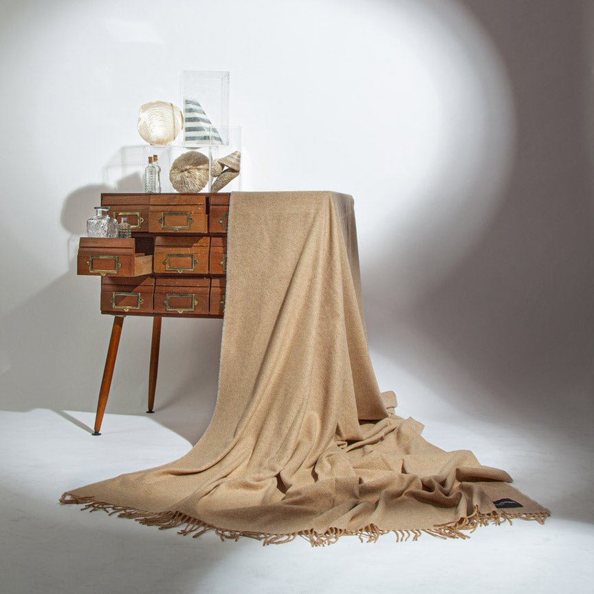 Beige blanket draped over a wooden side table with decorative items on a white background