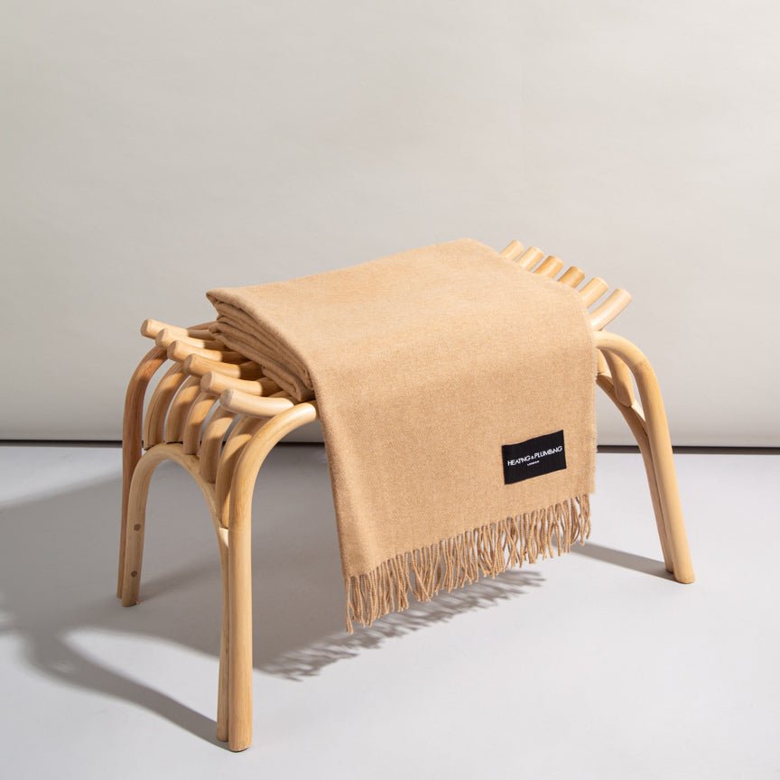 Beige blanket draped over a wooden stool with a visible brand label on a light gray background