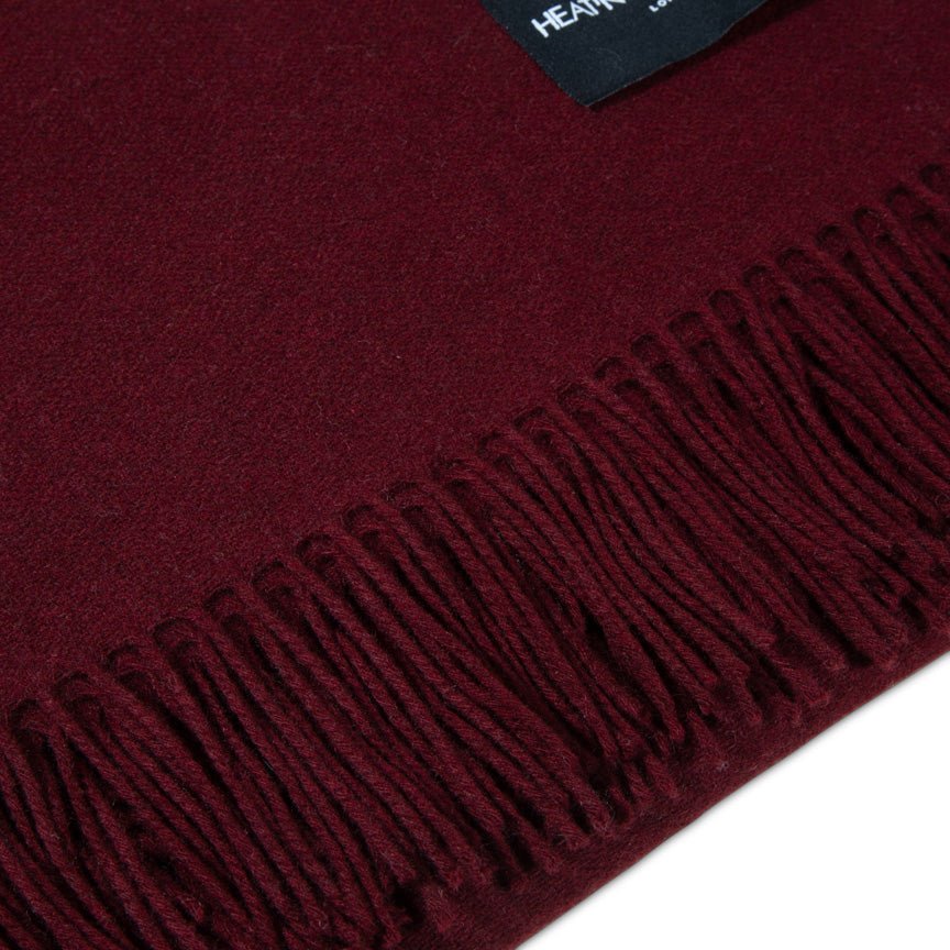 Close-up of a burgundy blanket with fringes on a white background