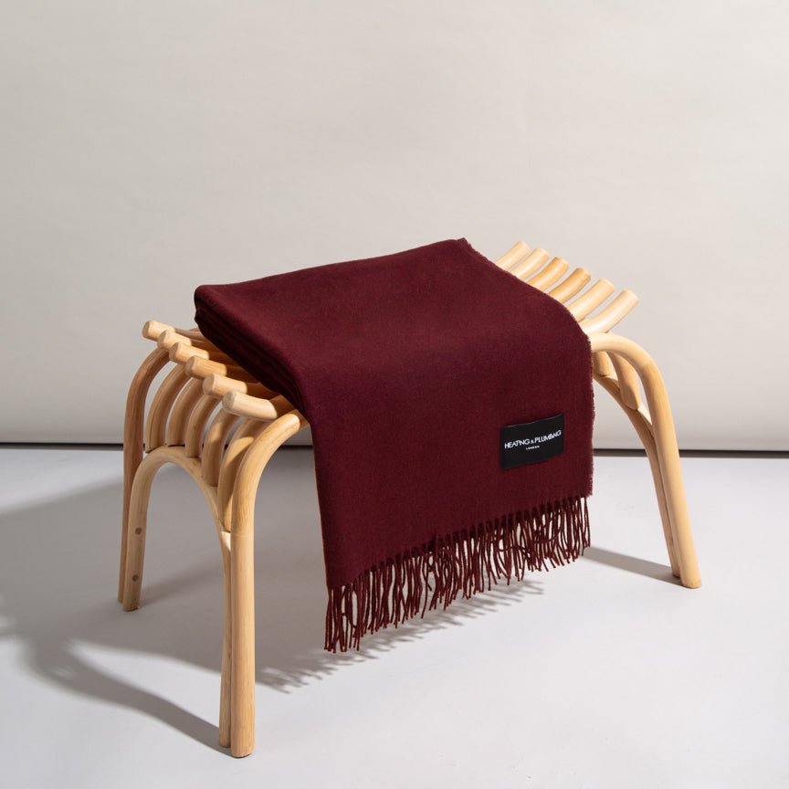 Maroon blanket with fringes draped over a wooden stool on a light background