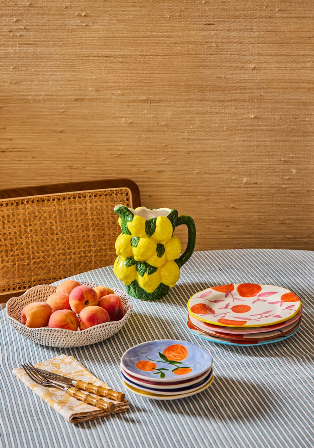 Ceramic pitcher with grapes, peach-themed plates, and a woven basket on a textured surface.