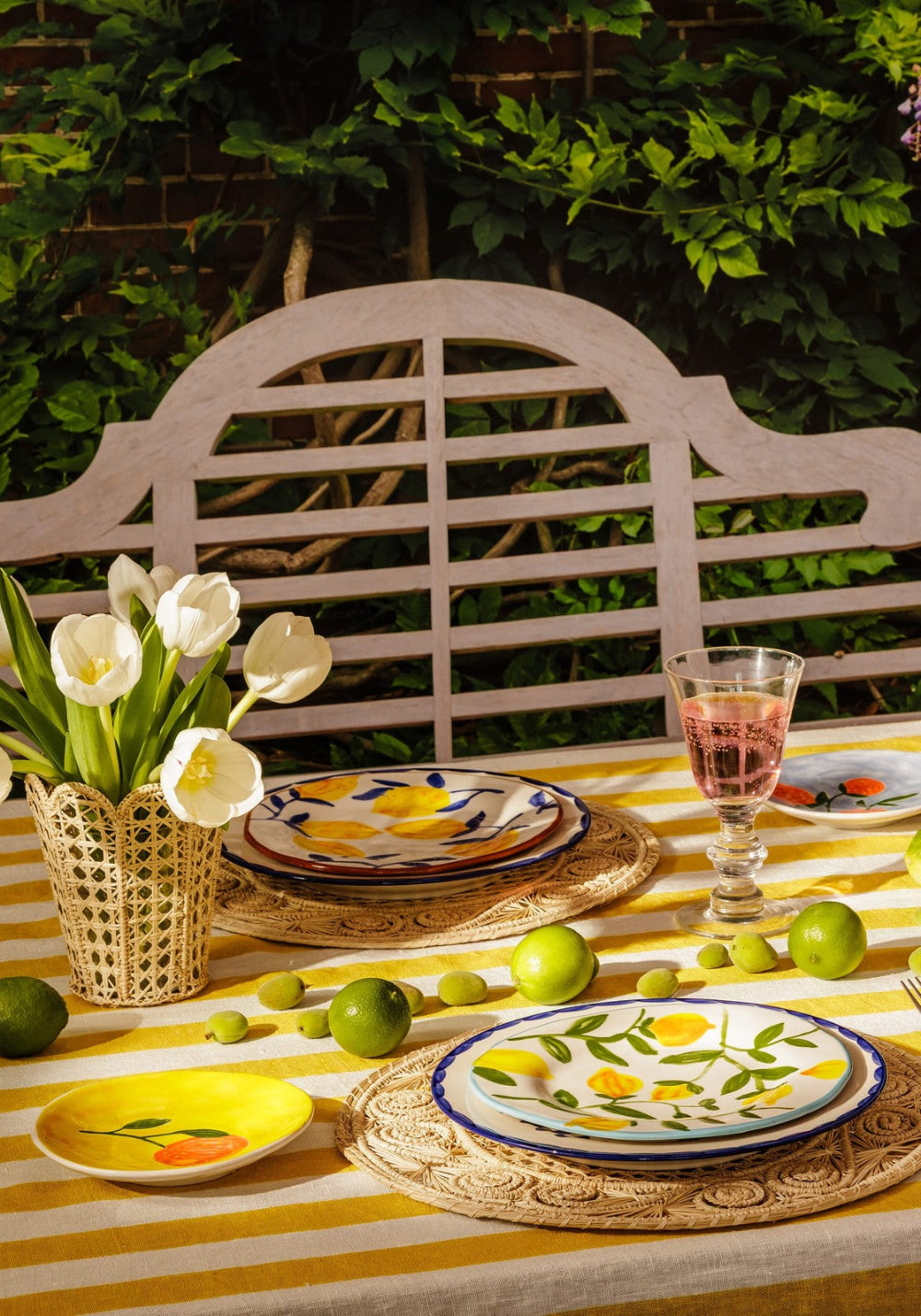 Outdoor table setting with floral arrangement, plates, and glasses on a striped tablecloth.