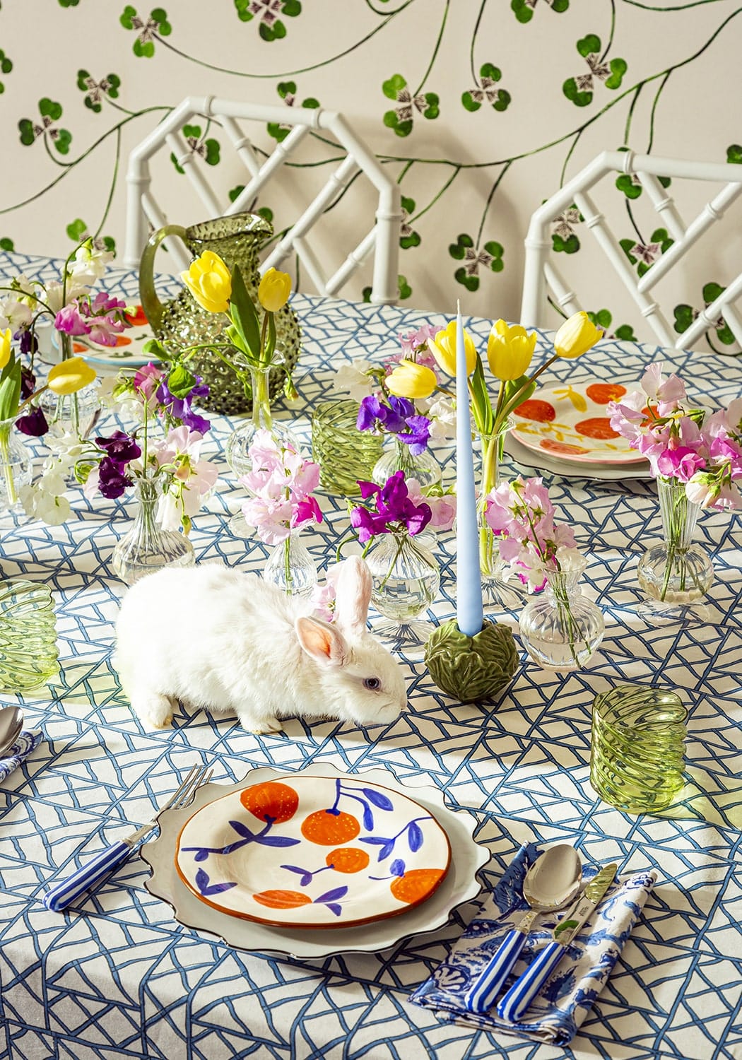Table setting with floral arrangements, a rabbit, and decorative plates on a patterned tablecloth.