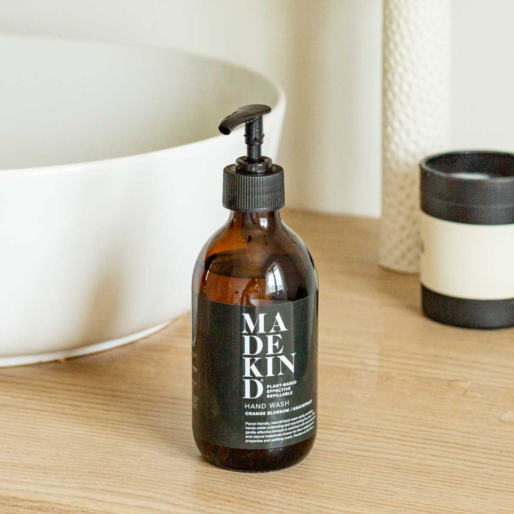 Brown bottle of Madkind hand wash on a wooden surface with a blurred background white sink in background of bathroom