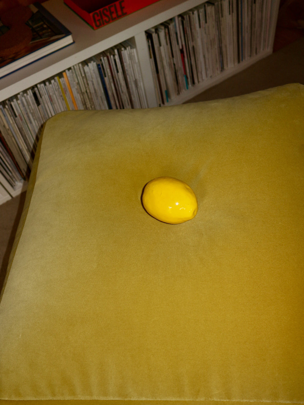 Yellow ceramic lemon on a yellow cushion with a bookshelf in the background
