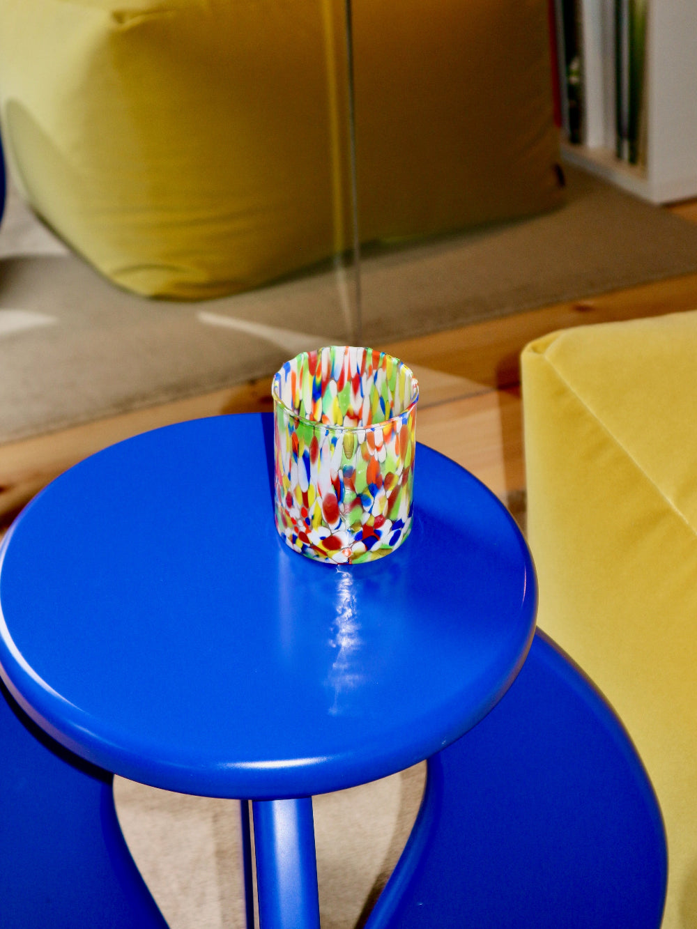 Colourful glass tumbler on a blue table with a yellow chair and green cushion in the background