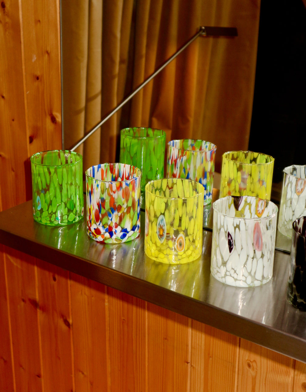 Coloruful murano glass tumblers on a wooden surface with a wooden wall background