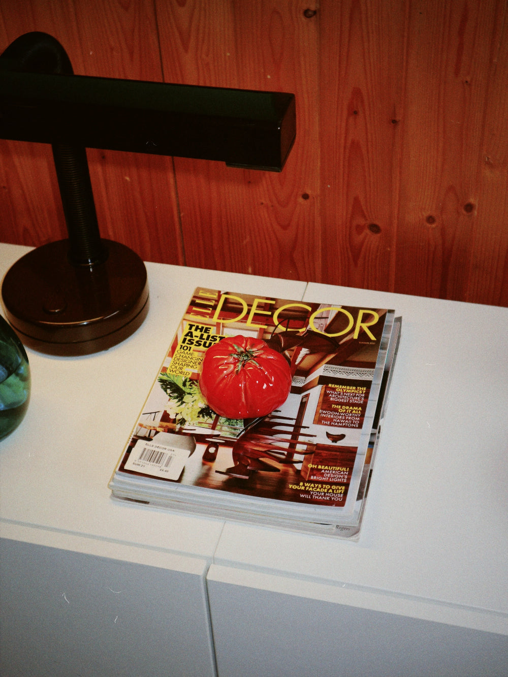 Magazine with a tomato on the cover on a white surface next to a black lamp.