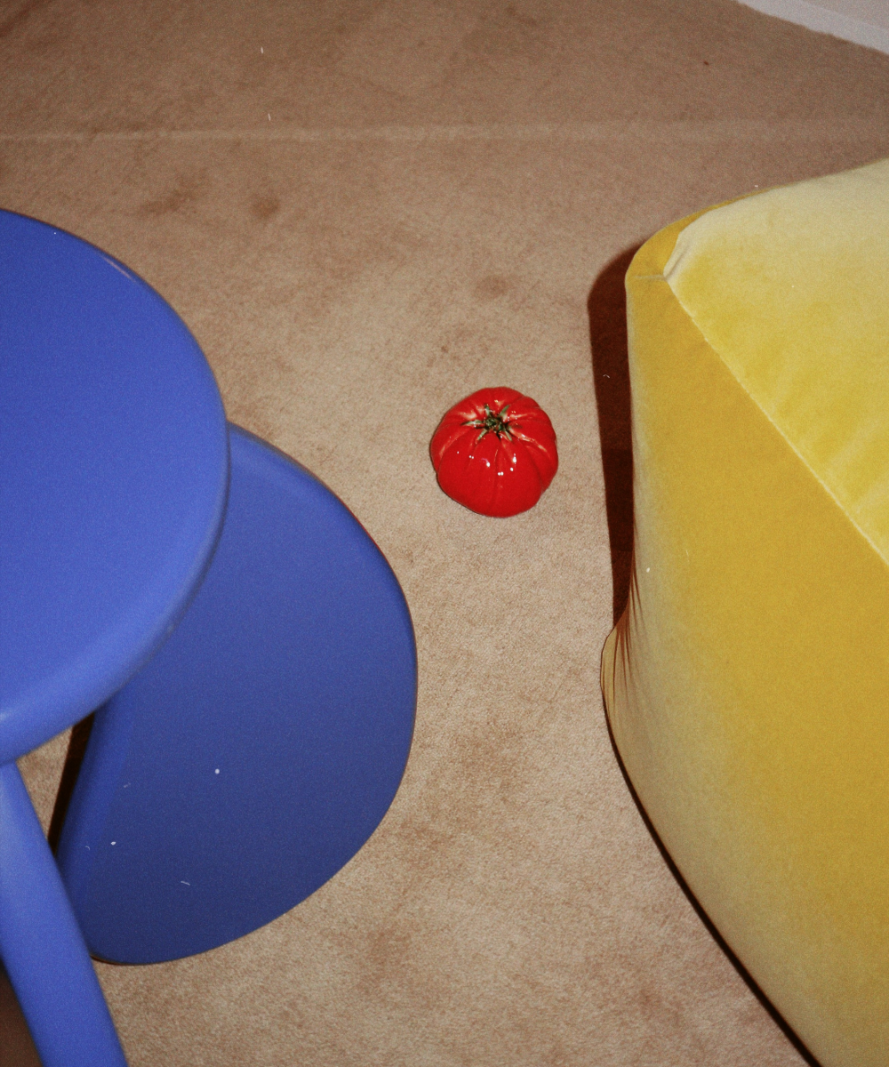 Small red tomato on a beige carpet next to a blue and yellow object