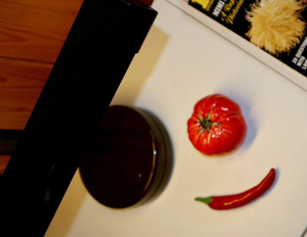 Tomato and red chili pepper on a white surface with a dark bottle in the foreground.