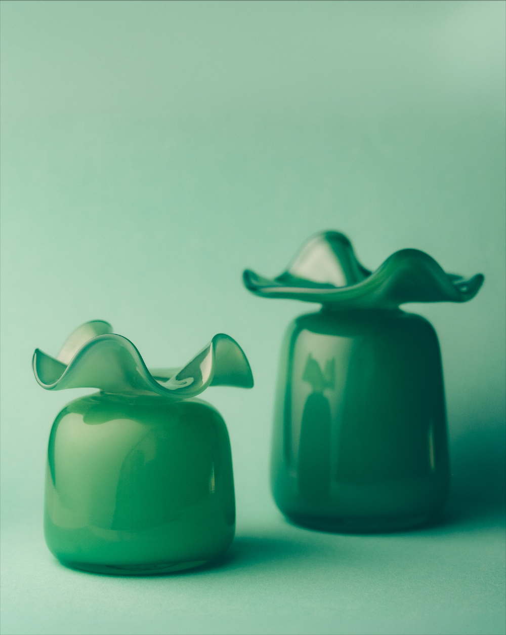 Two green glass vases with wavy designs on a light green background