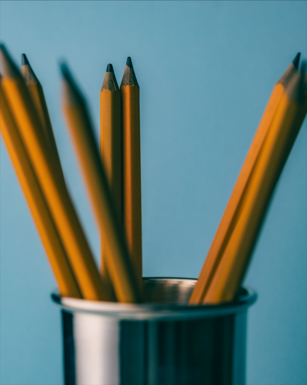 Pencils in silver plate bud vase with pencils on a blue background