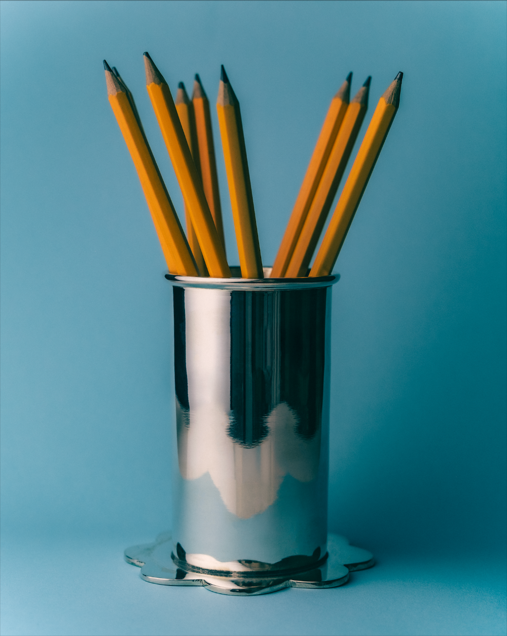 Silver scallop pot filled with yellow pencils against a blue background