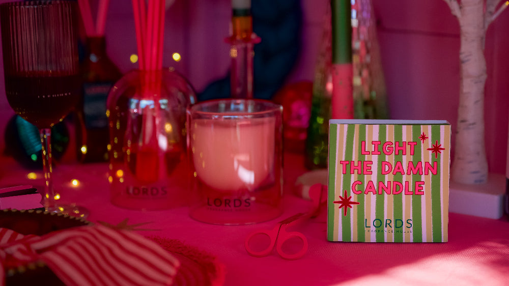 Candle with 'LORDS' branding on a pink surface, surrounded by decorative items.