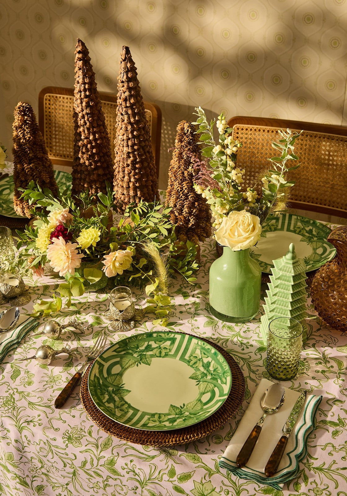 Decorative table setting with green plates, floral arrangements, and decorative trees on a patterned tablecloth.