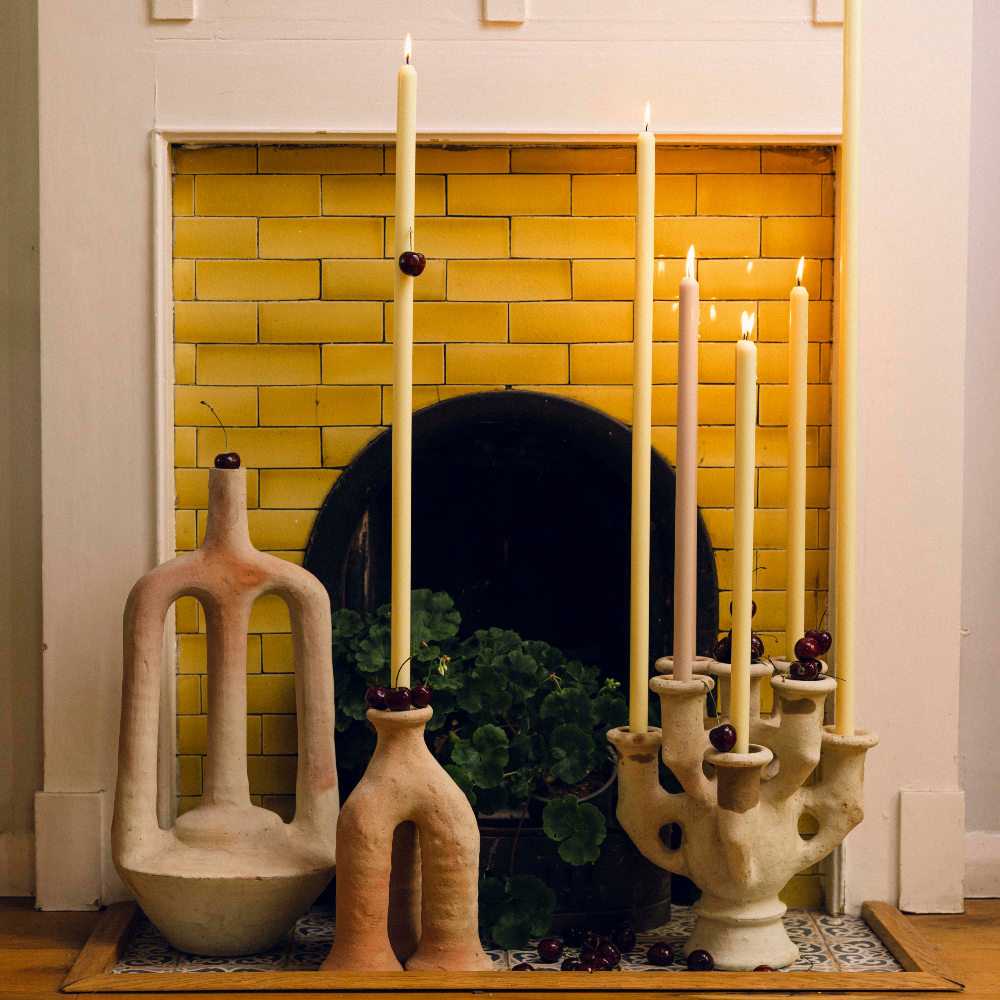 Decorative metre long candles and ceramic holders in front of a yellow-tiled fireplace.