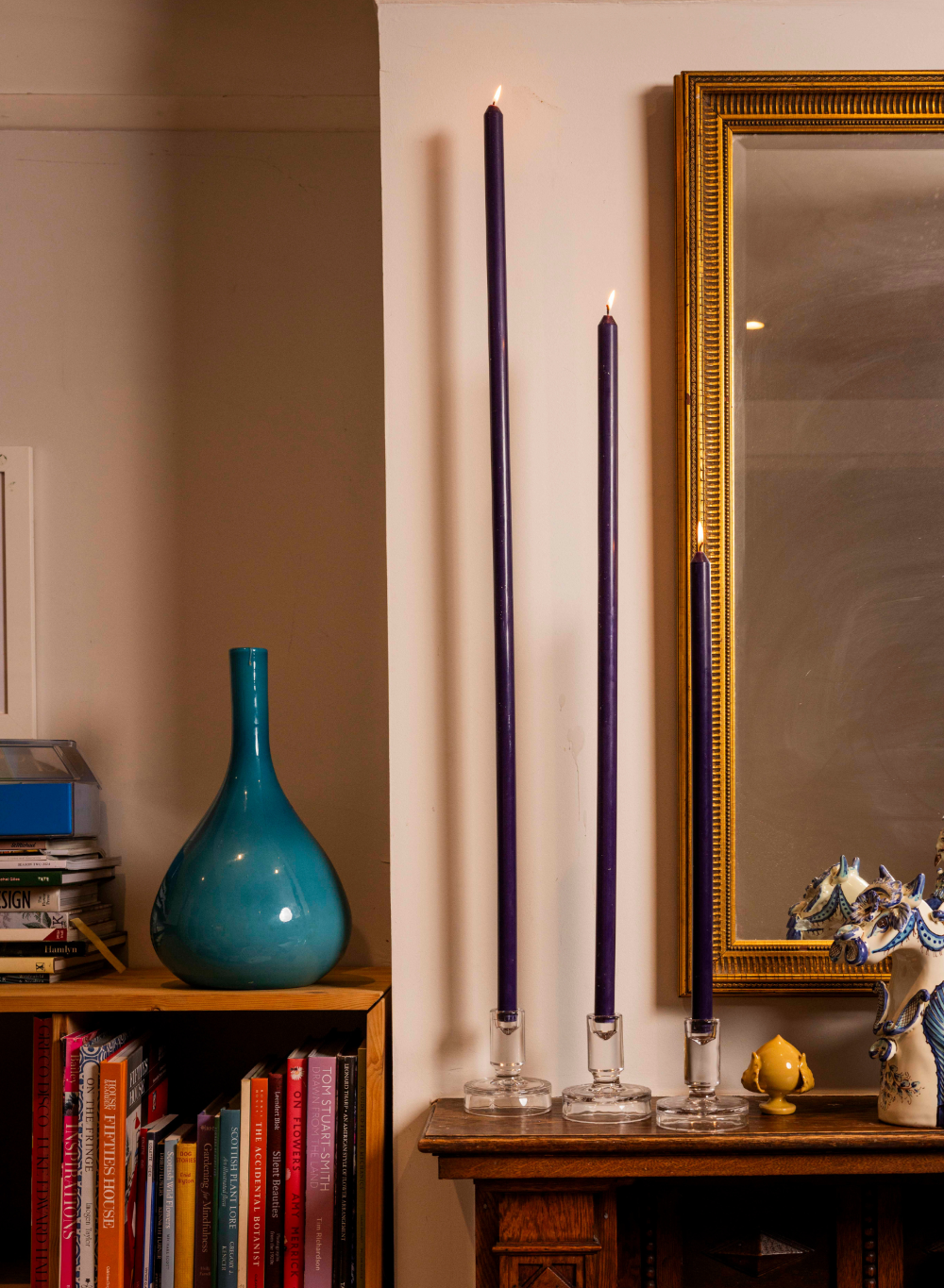 Decorative setup with a blue vase, tall purple candles, and a gold-framed mirror on a wall.