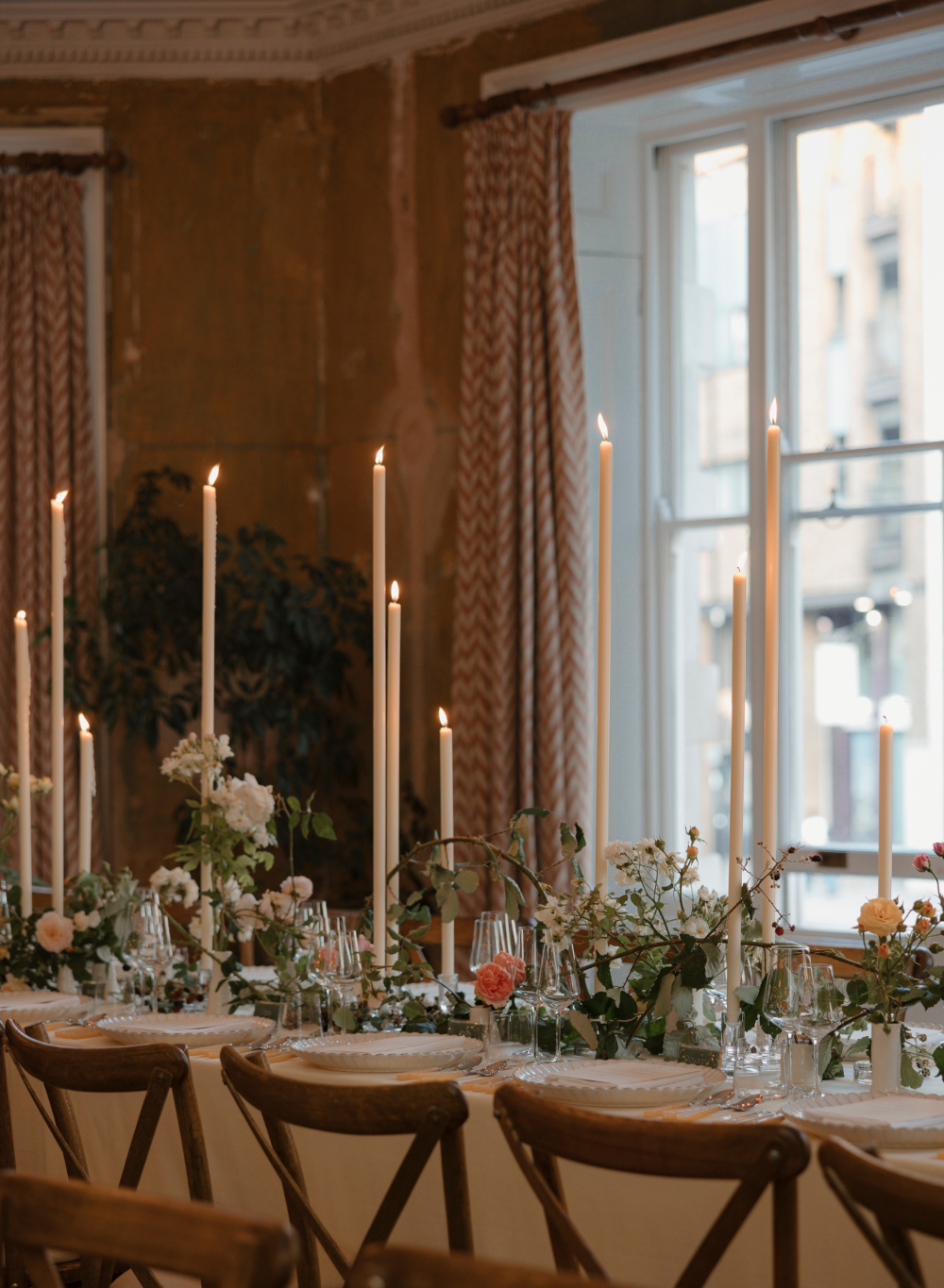 Elegant dining table setting with candles and floral arrangements in a room with large windows.