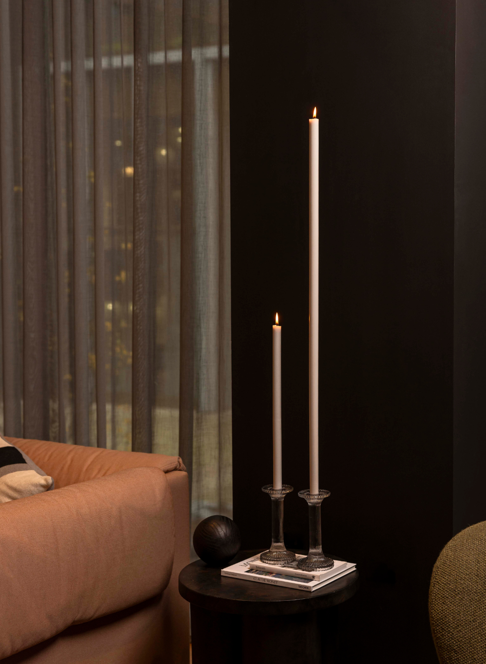 Two candlesticks with lit candles on a small table against a dark wall.