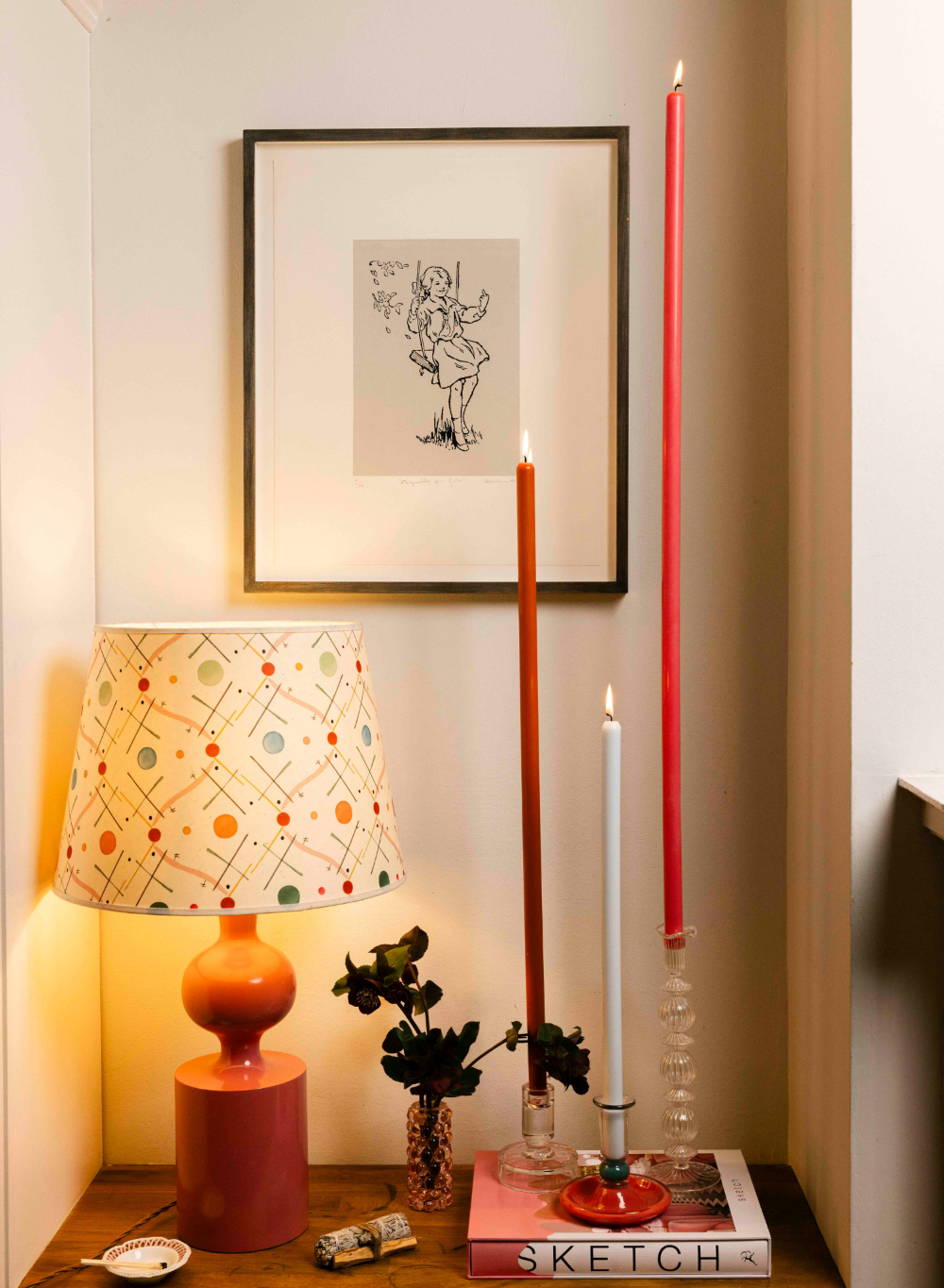 Decorative setup with a lamp, candles, and framed artwork on a wall.