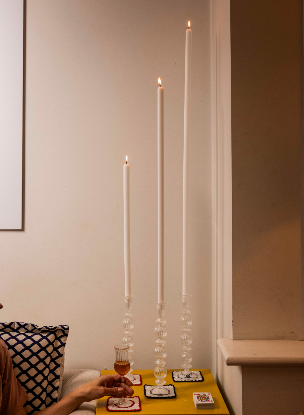 Candlelit scene with a glass of red wine on a small table against a neutral wall.