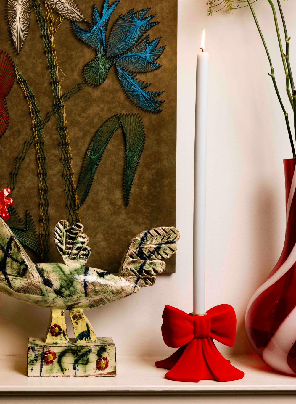 Decorative candle with red holder on a surface with floral embroidery in the background