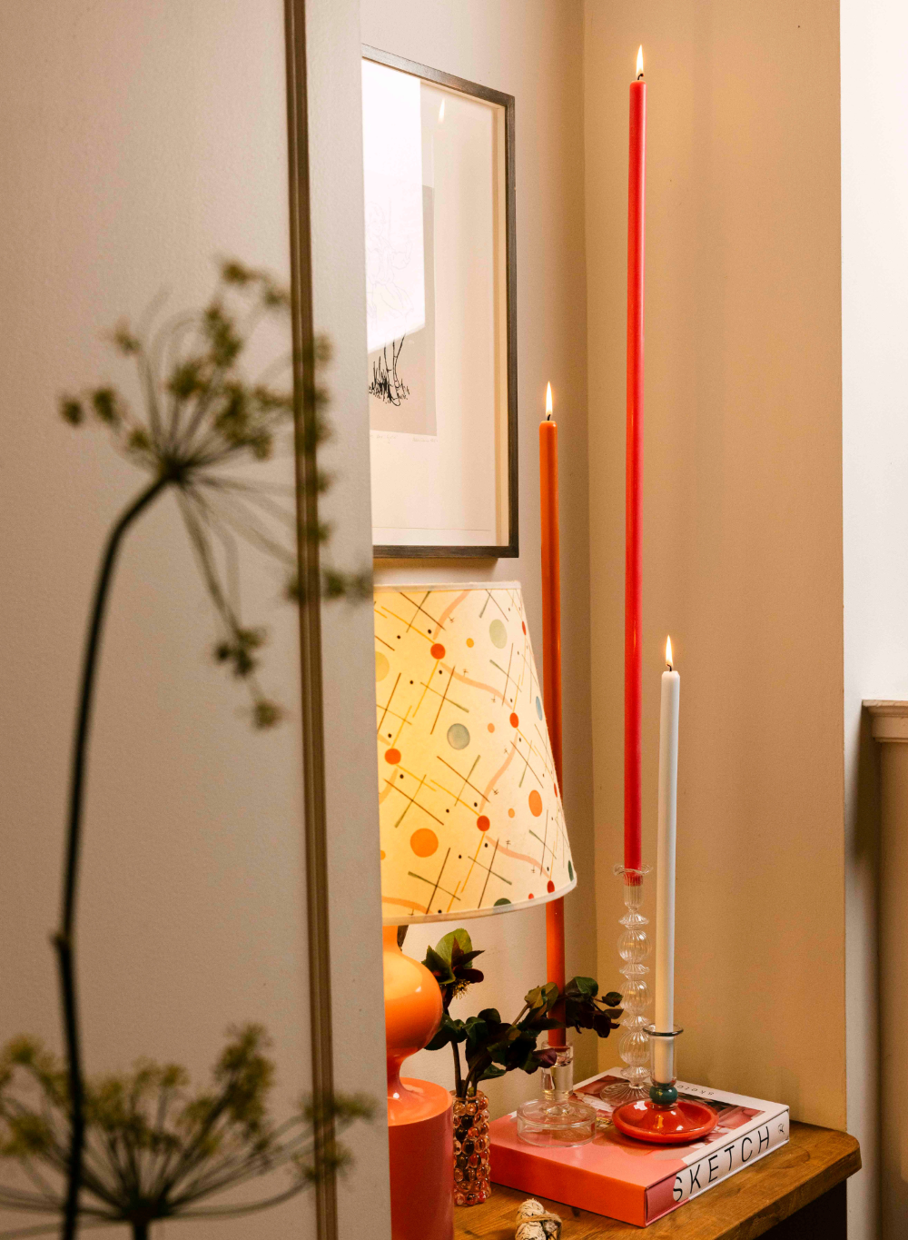 Decorative setup with candles, a lamp, and books on a shelf.