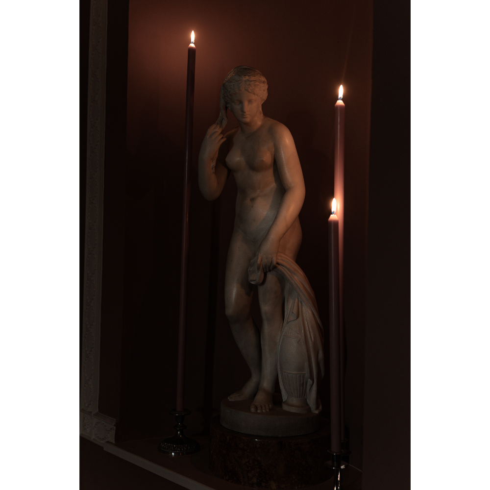 Statue of a nude figure in a dimly lit room with candles