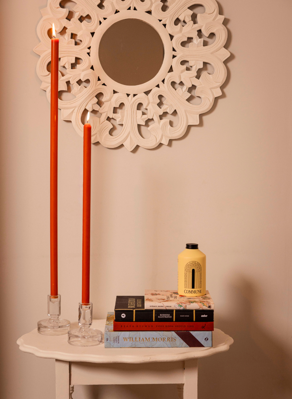 Decorative setup with red candles, books, and a decorative mirror on a beige wall.