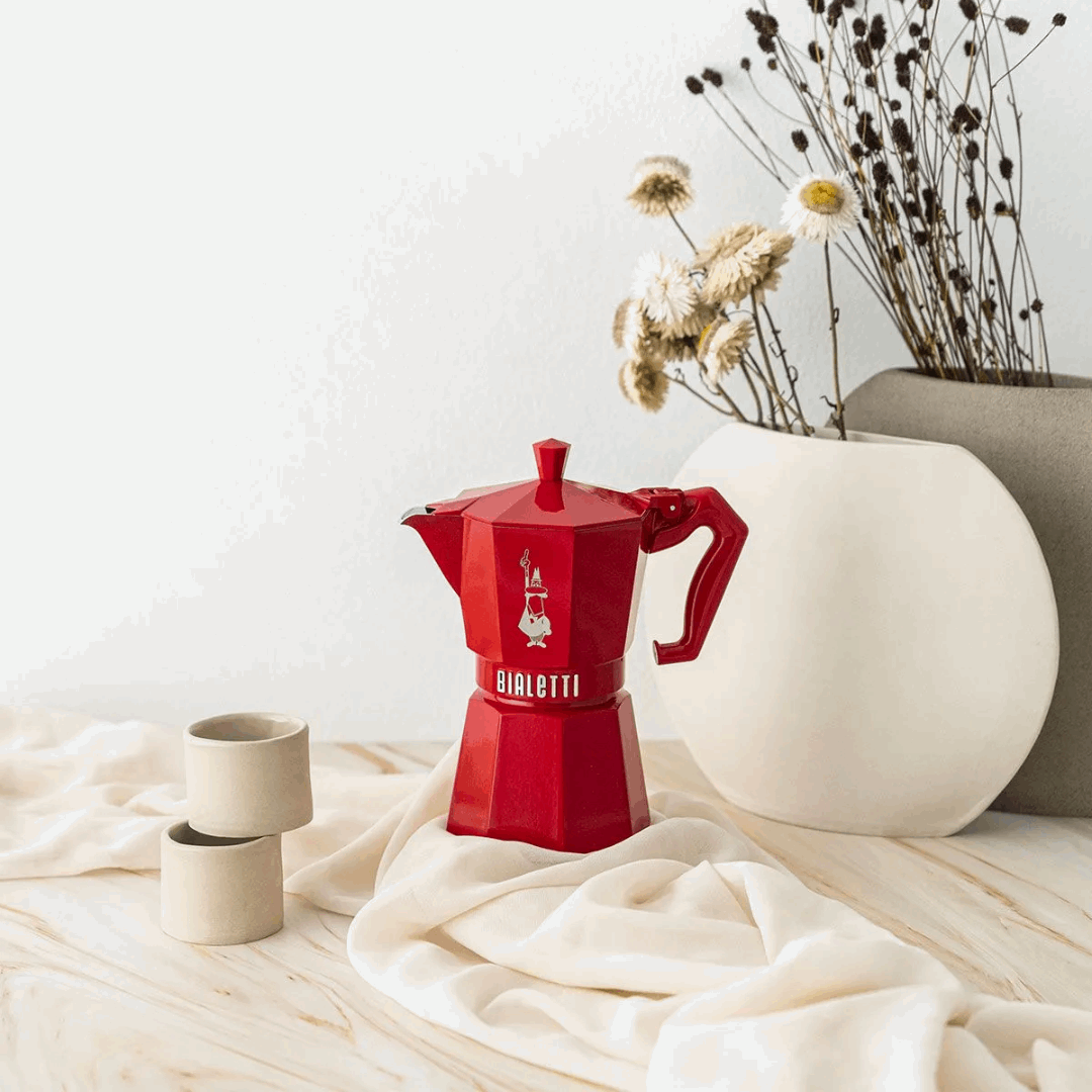 Red Bialetti coffee maker on a light surface with decorative elements.