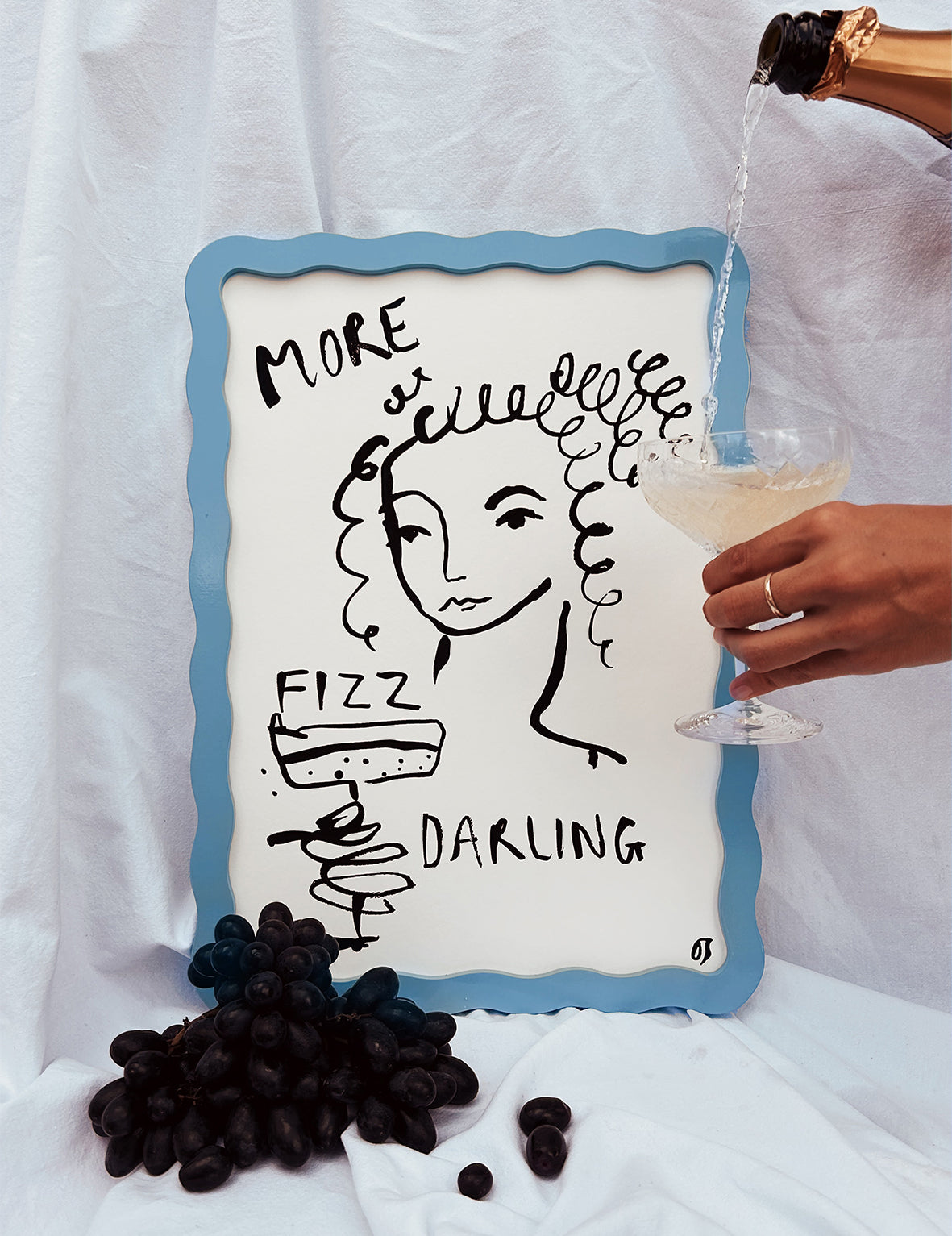Decorative sign with a woman's face and text, accompanied by grapes and a glass of champagne.