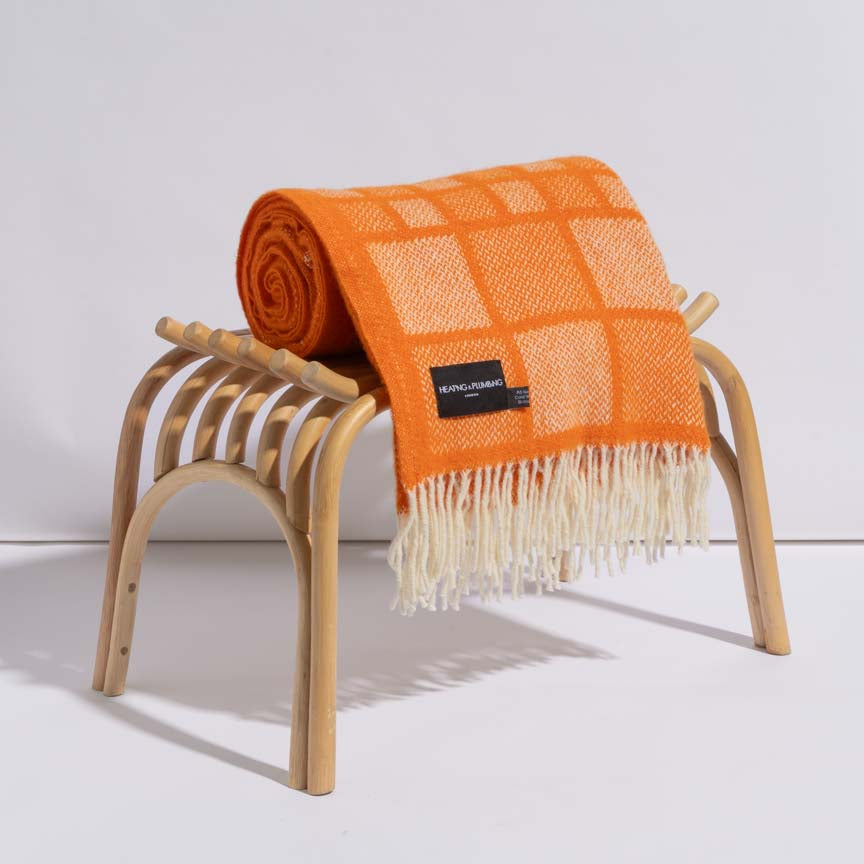 Orange checkered blanket with fringes draped over a wooden stool on a white background