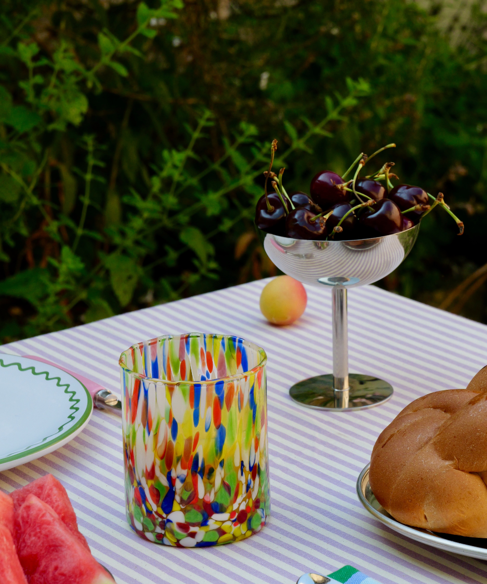Colourful murano glass on a striped tablecloth with fruit and bread in the background