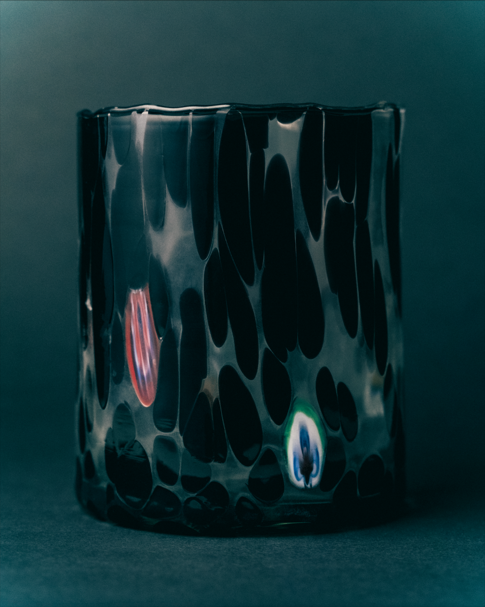 Black glass murano tumbler with abstract patterns on a dark background