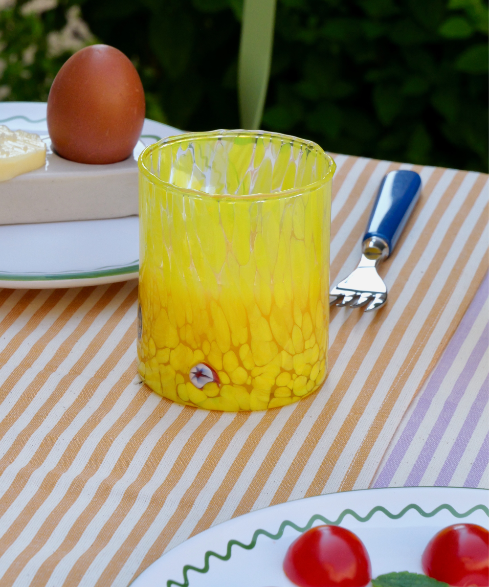 Yellow textured glass tumbler on a striped tablecloth with an egg and fork in the background.