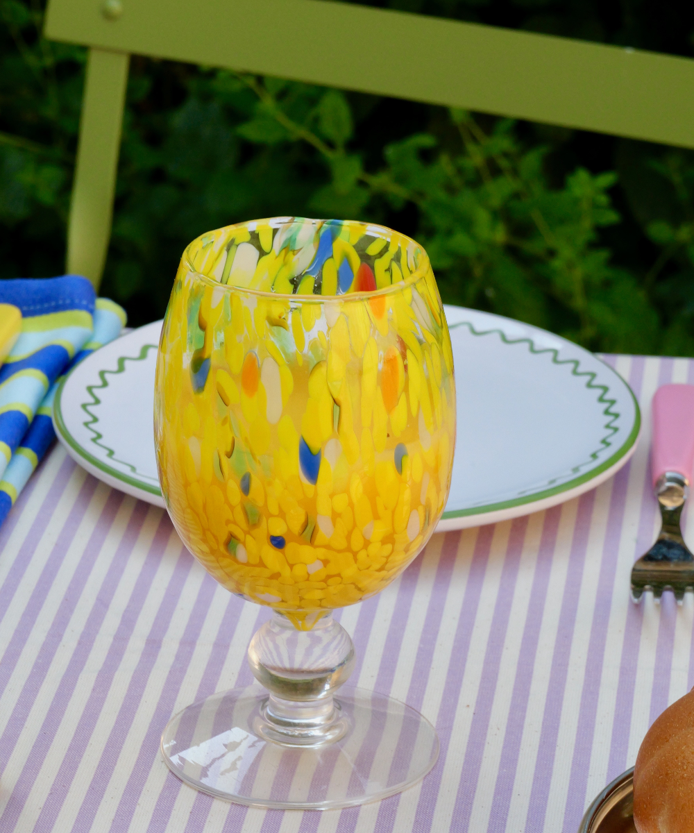 Colourful murano wine glass on a striped tablecloth with outdoor background