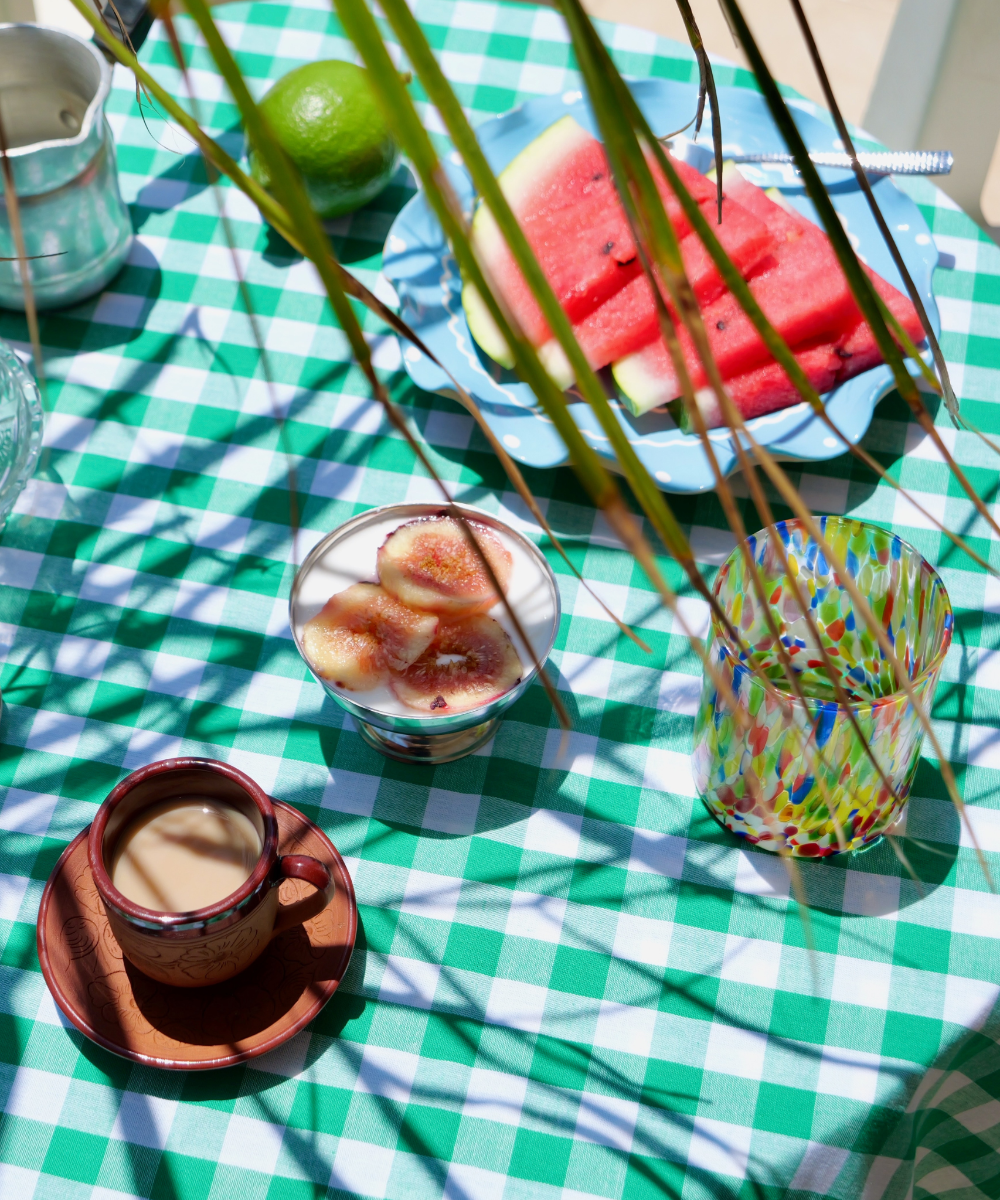 Outdoor setting with a green and white checkered tablecloth, watermelon slices, and a colourful glass.