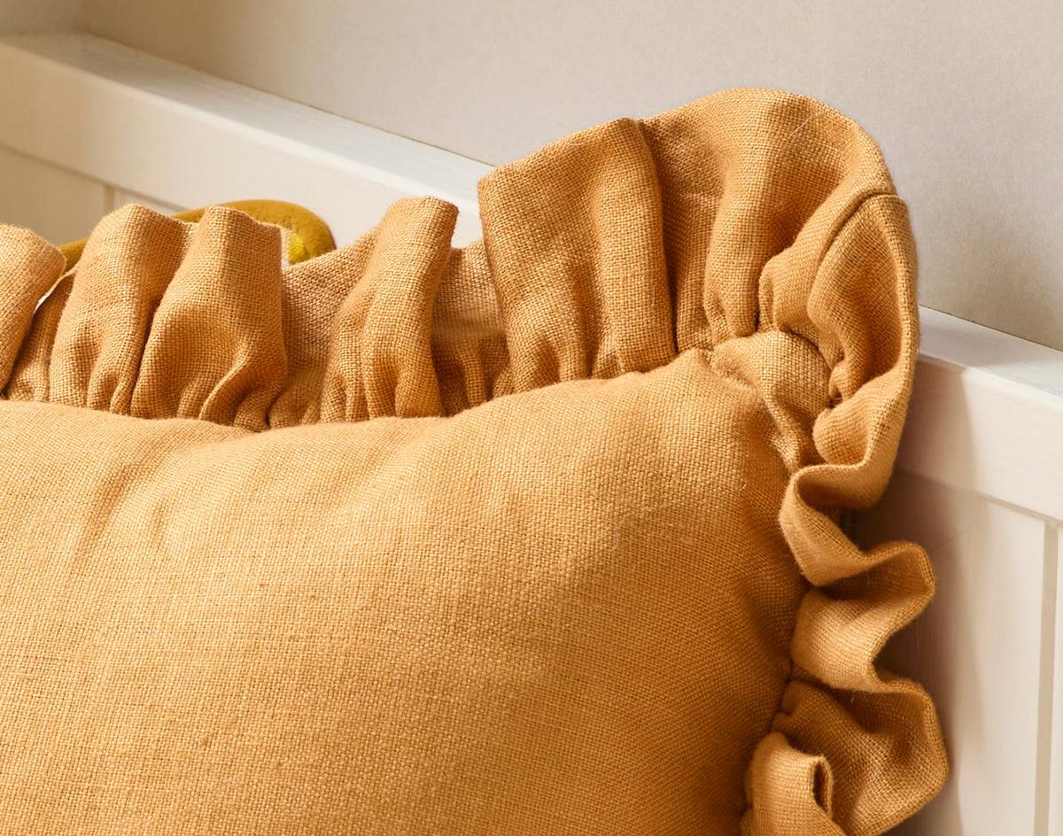 Mustard yellow cushion with ruffled edge on a white background