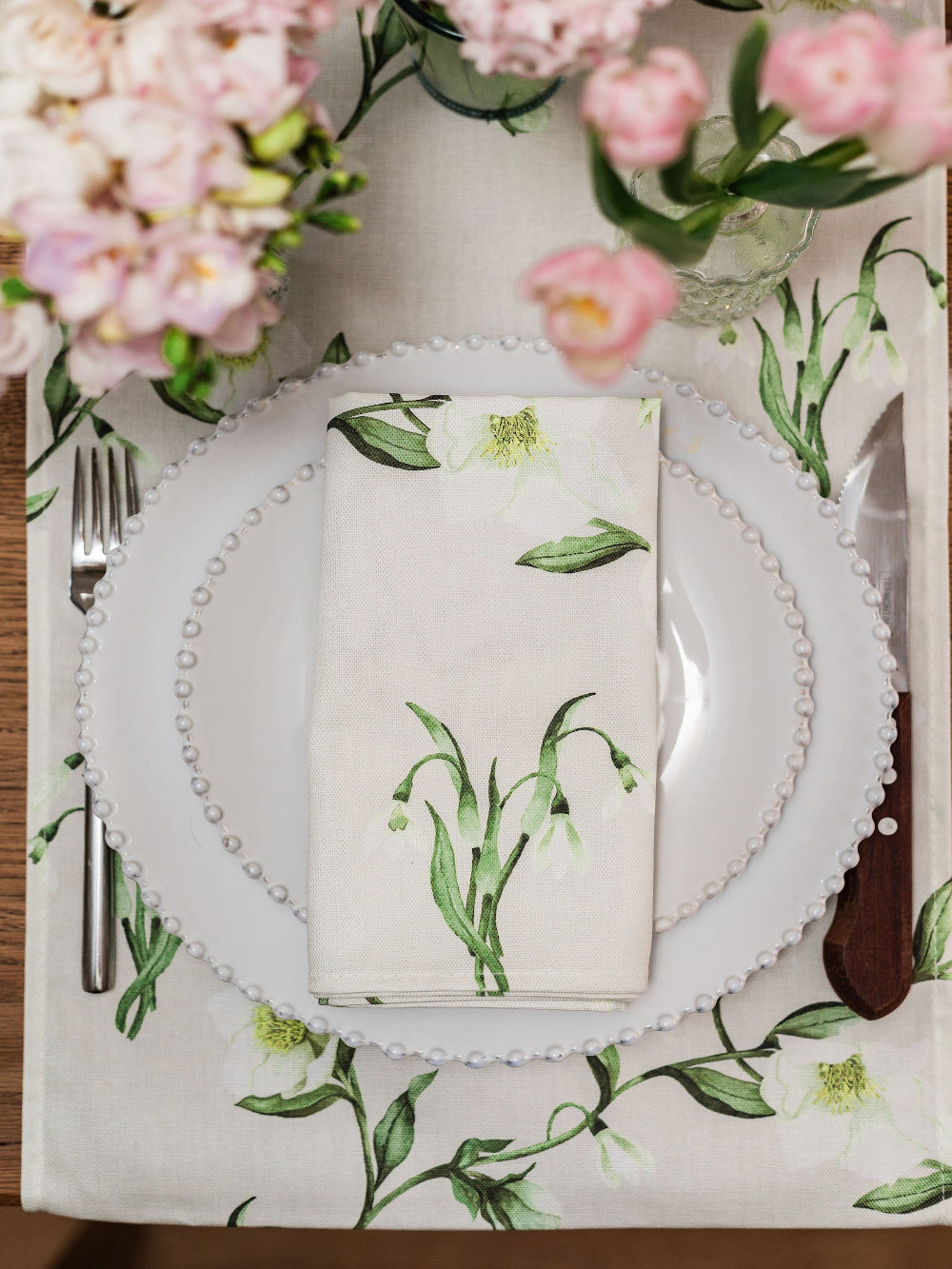 Table setting with floral tablecloth, white plate, and napkin with green leaf pattern.