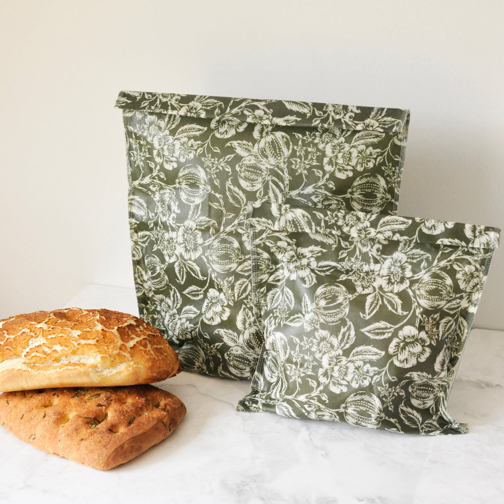 Two floral-patterned beeswax food storage bags and two loaves of bread on a white surface.
