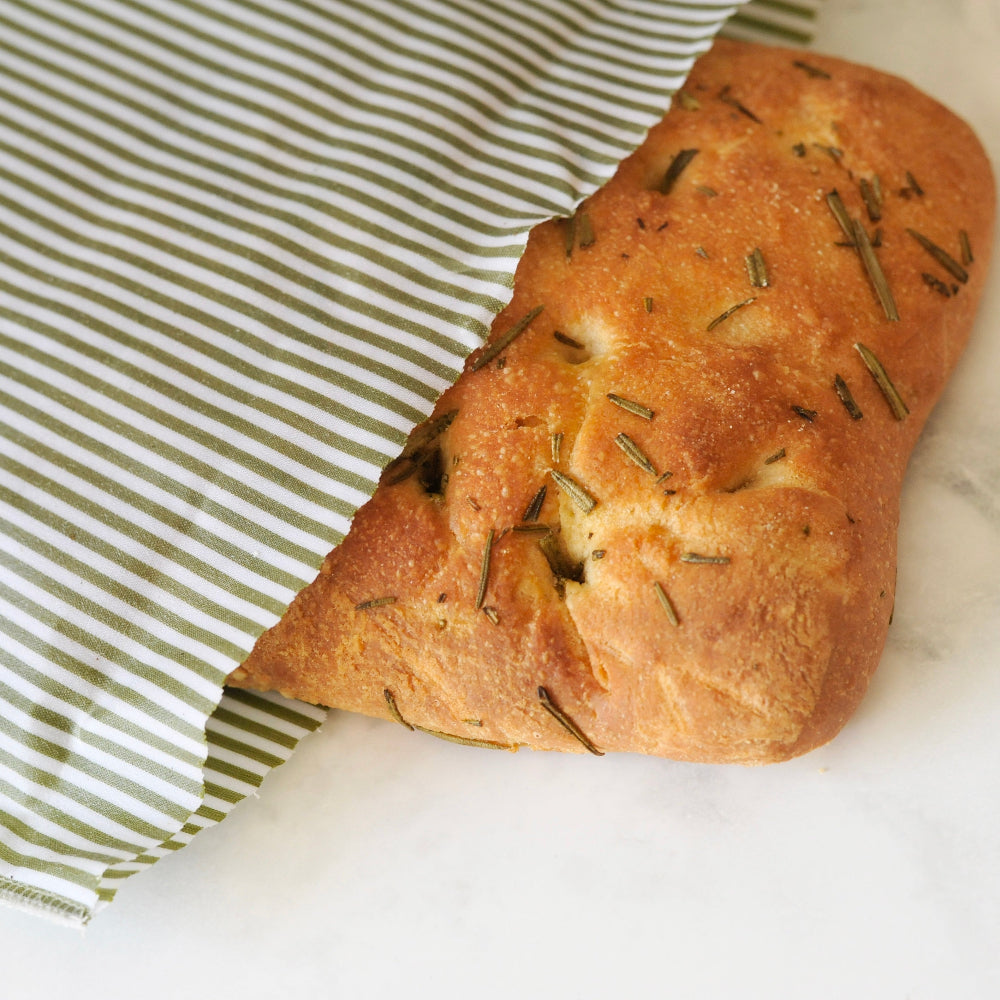 Loaf of bread with rosemary on a white surface with a green striped beeswax food bag