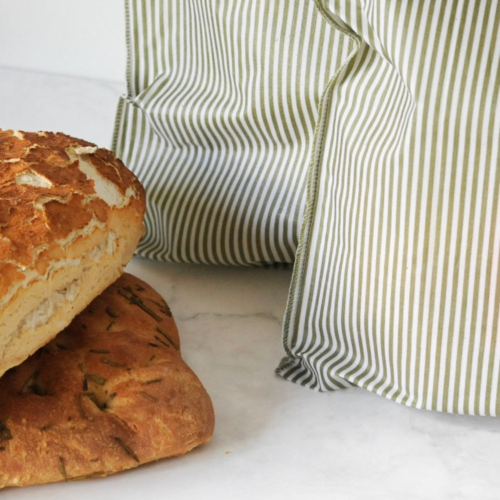 Two loaves of bread with a green and white striped beeswax food storage bags on a white surface