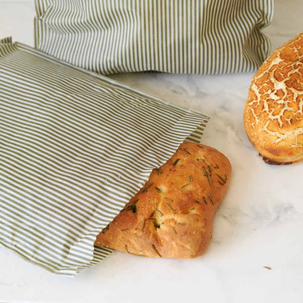 Loaf of bread on a marble surface with striped green beeswax food bags.