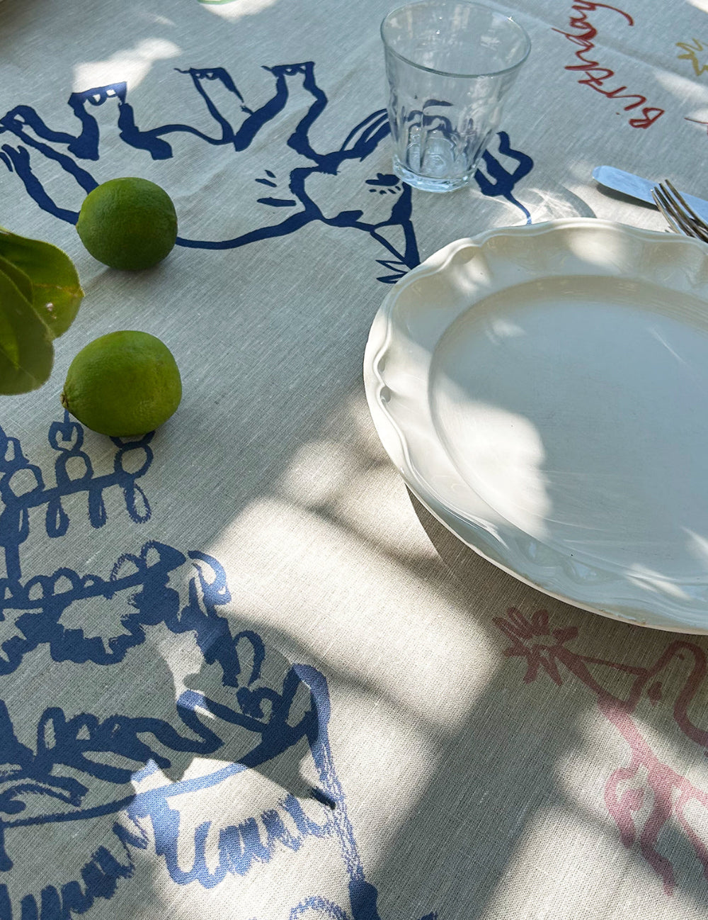 Table setting with a white plate, glass, and green apples on a decorative tablecloth.