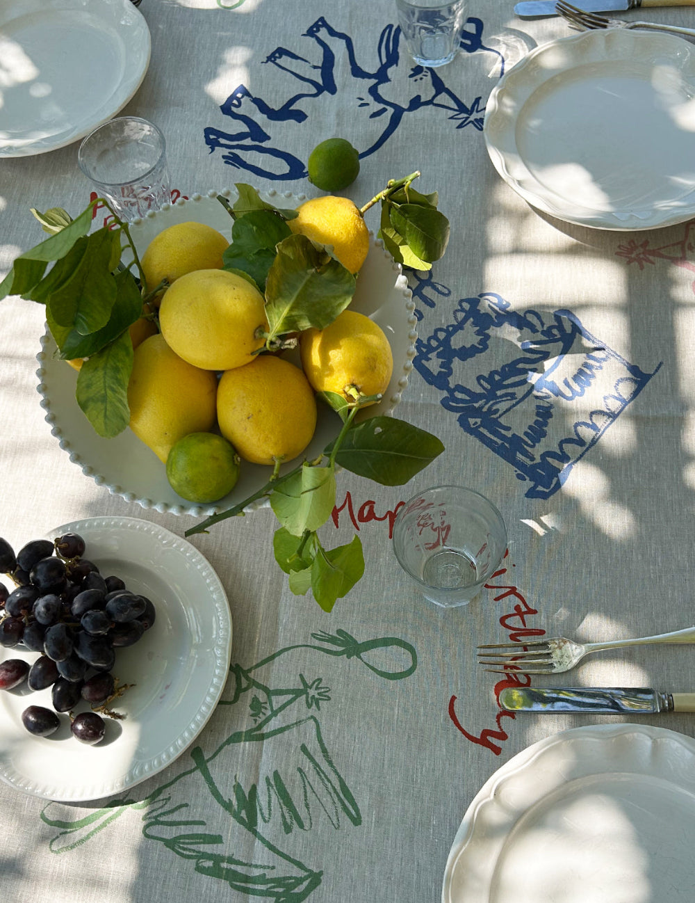 Table setting with lemons, grapes, and cutlery on a decorative tablecloth.