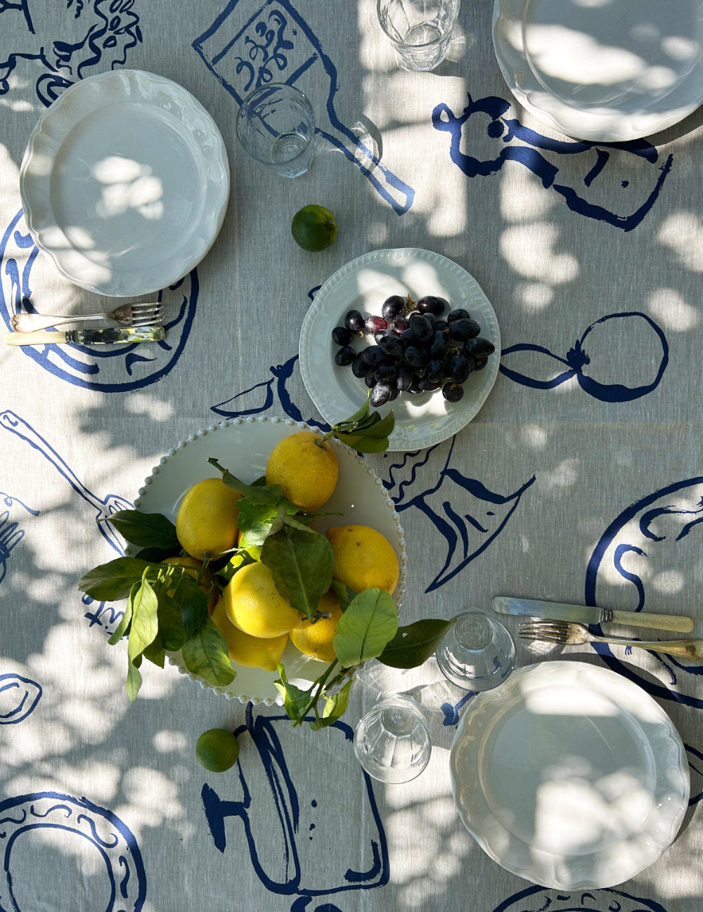Table setting with lemons, grapes, and white plates on a decorative tablecloth.